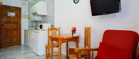 A compact living space with a kitchenette, a dining area with wooden furniture, and a red sofa.