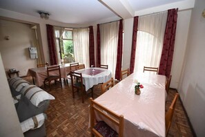 A dining area with a round table, chairs, a sofa, and a window with curtains. - Weygoss Guest House (Addis Ababa)