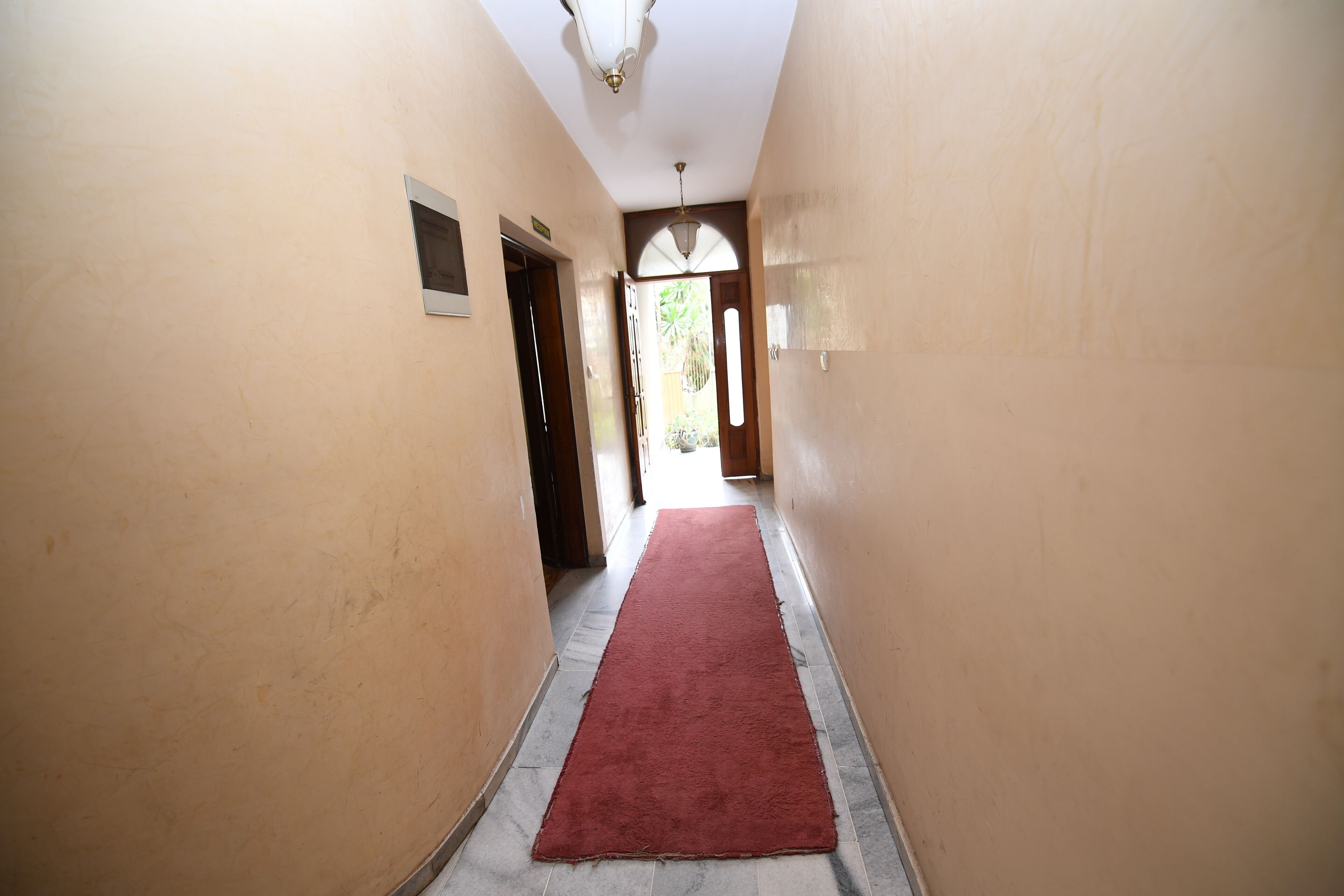 A hallway with a red carpet, beige walls, and a ceiling light fixture.