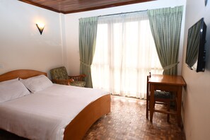 A bedroom with a large bed, a wooden table, a chair, and a TV on the wall. - Weygoss Guest House (Addis Ababa)
