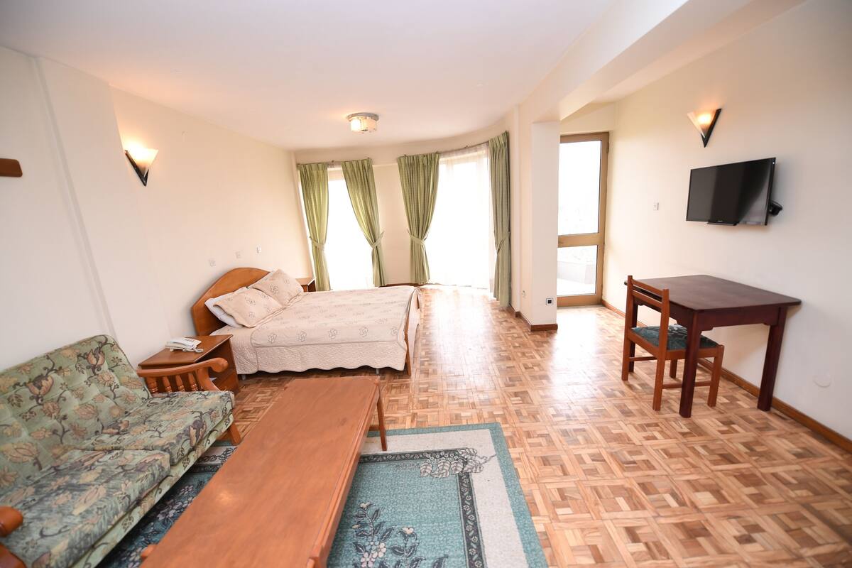 A bedroom with a bed, a sofa, a table, and a TV.