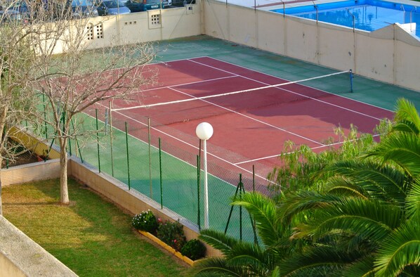 Una cancha de tenis con red, rodeada por una valla y palmeras.