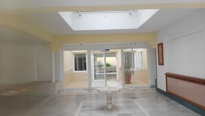 Eine großzügige Lobby mit hoher Decke, einem zentralen Brunnen und Blick ins Freie durch Glasüren.
