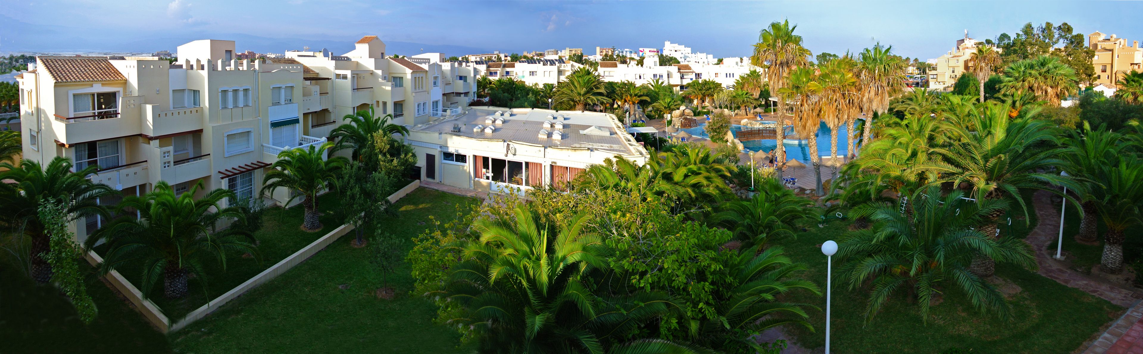Zona residencial con modernos edificios de apartamentos, piscina y abundante vegetación.
