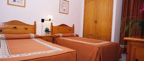 A hotel room with two beds, a wooden wardrobe, a nightstand with a lamp, and a framed picture on the wall.