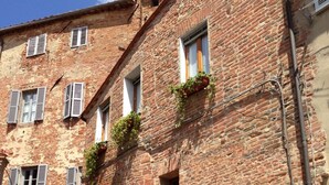 Un edificio histórico de ladrillo con varias ventanas, algunas con contraventanas y algunas con macetas.