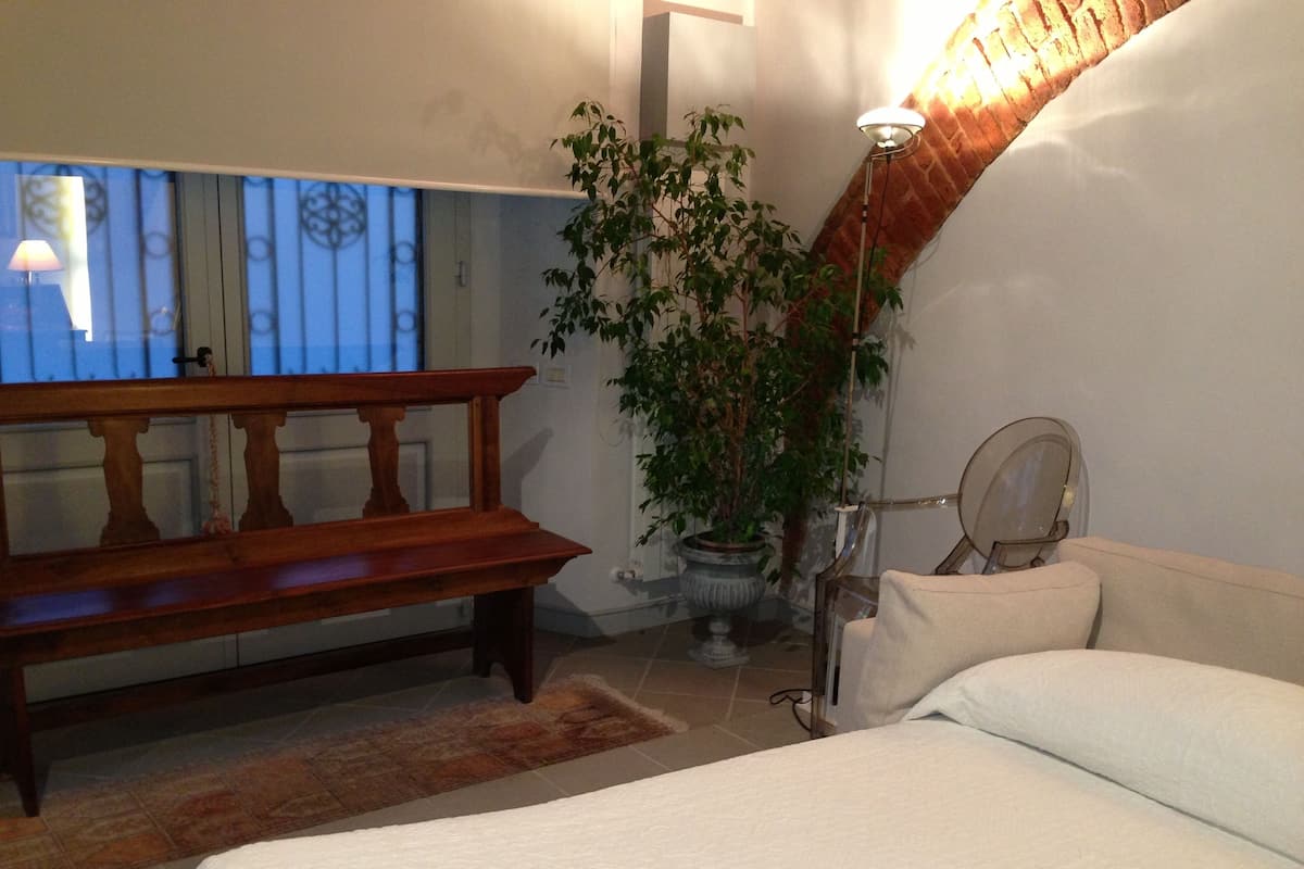A bedroom with a bed, a bench, a potted plant, and a mirror.