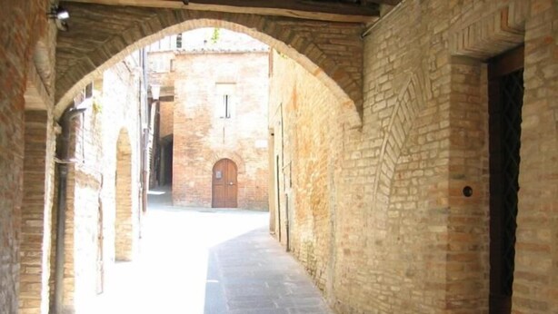 Un corredor de piedra con arco y un edificio de ladrillo al fondo.