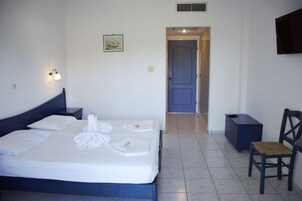Habitación de hotel con cama, una silla, escritorio, televisor montado en la pared y puerta que da a otra habitación.