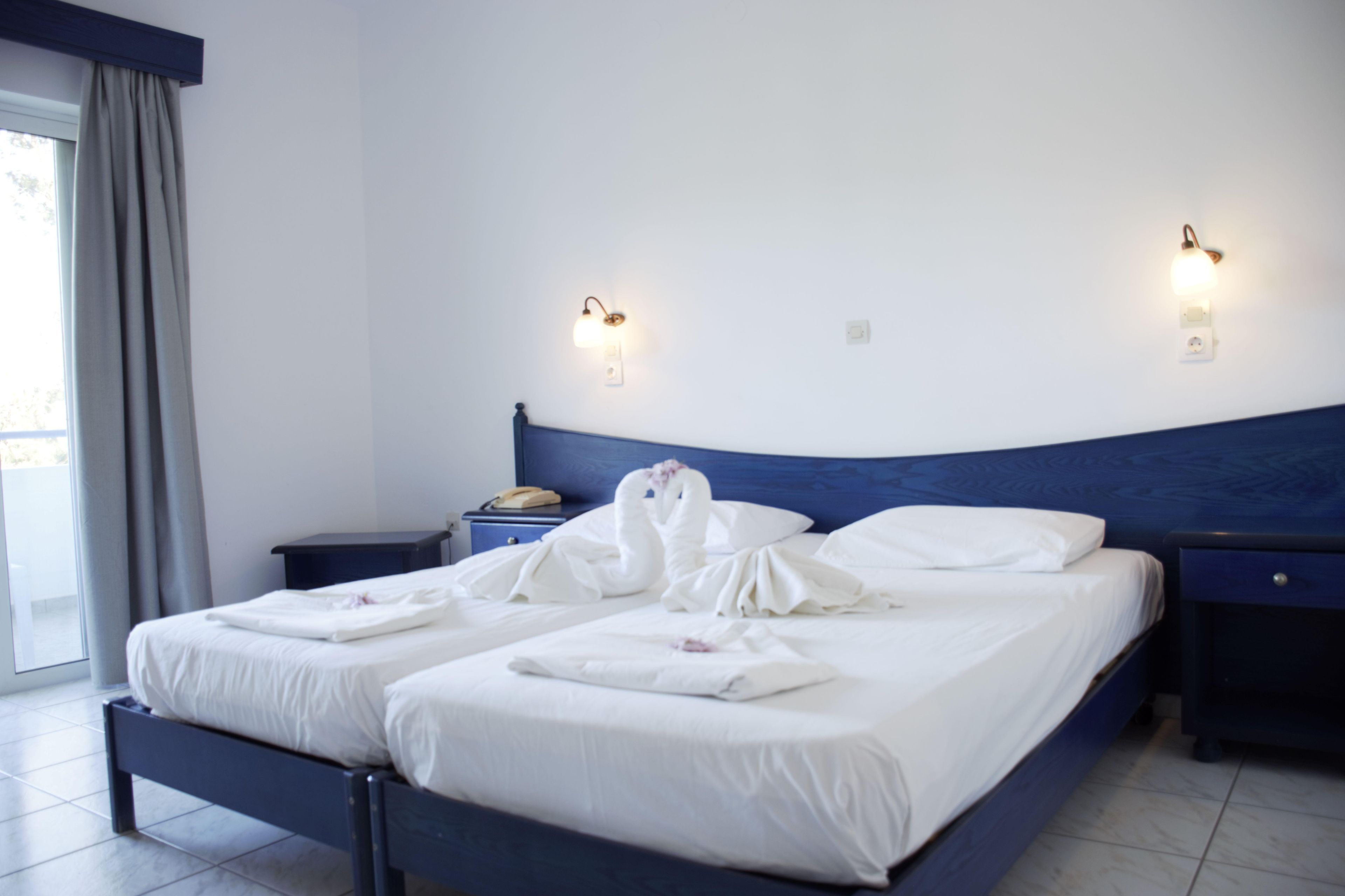 Ein Hotelzimmer mit einem Bett, zwei Nachttischen, einer Wandlampe und einem Fenster mit Vorhängen.