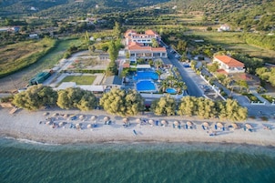 Vista aérea de un hotel frente al mar, con piscina, playa y exuberante vegetación.