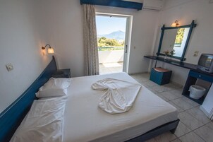 Habitación de hotel con cama, escritorio con computadora, espejo y vista al exterior.