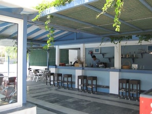 Un área de bar al aire libre con mostrador, taburetes y una persona atendiendo.