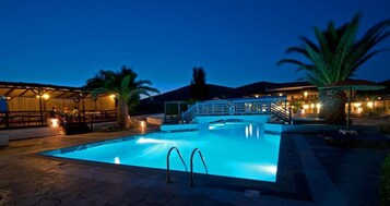 A swimming pool with a bridge, palm trees, and a building with lights.