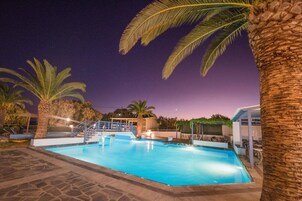 Una piscina con una escalera que lleva a una zona cubierta, rodeada de palmeras y un sendero de piedra.