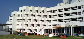Un immeuble à plusieurs étages doté de balcons, d’un espace extérieur aménagé avec des sièges, et d’une zone couverte avec des tables et des chaises.