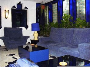 Una habitación con un sofá azul, una mesita con una lámpara y una ventana con cortinas azules.