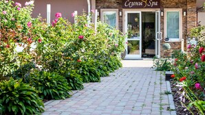L’entrée d’un spa, avec un chemin en briques menant à la porte, est bordée d’une végétation luxuriante et de plantes en fleurs.