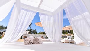 Un espace de détente extérieur baigné de lumière, avec des rideaux blancs, une piscine et des chaises longues.