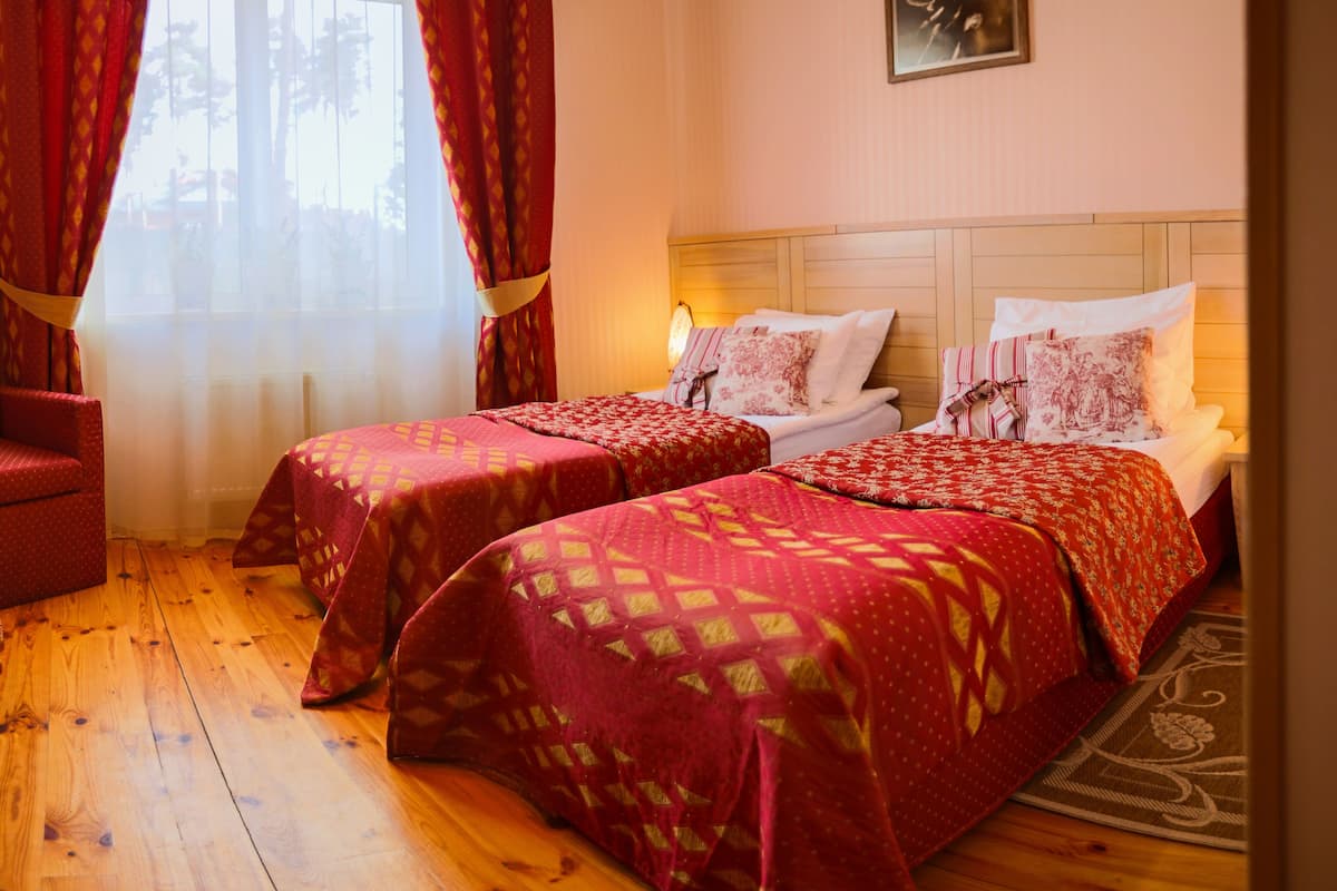 Hotellihuone, jossa on kaksi sänkyä, puulattia ja ikkuna, jossa on punaiset verhot.