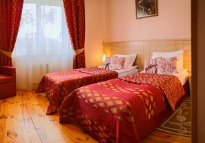 Habitación de hotel con dos camas, piso de madera y una ventana con cortinas rojas.