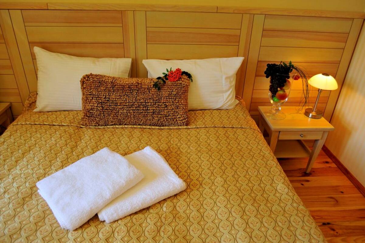 Hotellihuone, jossa on sänky, kaksi tyynyä, yöpöytä lampun kanssa ja maljakko, jossa on kukkia.