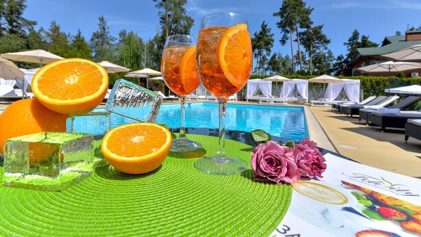 Une scène au bord de la piscine avec deux verres de jus d’orange, des glaçons et une rose posée sur un tapis vert.
