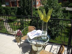 Un balcón con sillas de mimbre, una mesa de vidrio y un florero con flores amarillas.