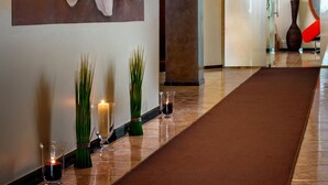 Un couloir orné d’une grande fresque florale, un vase en verre contenant des plantes vertes et des bougies posées sur le sol.