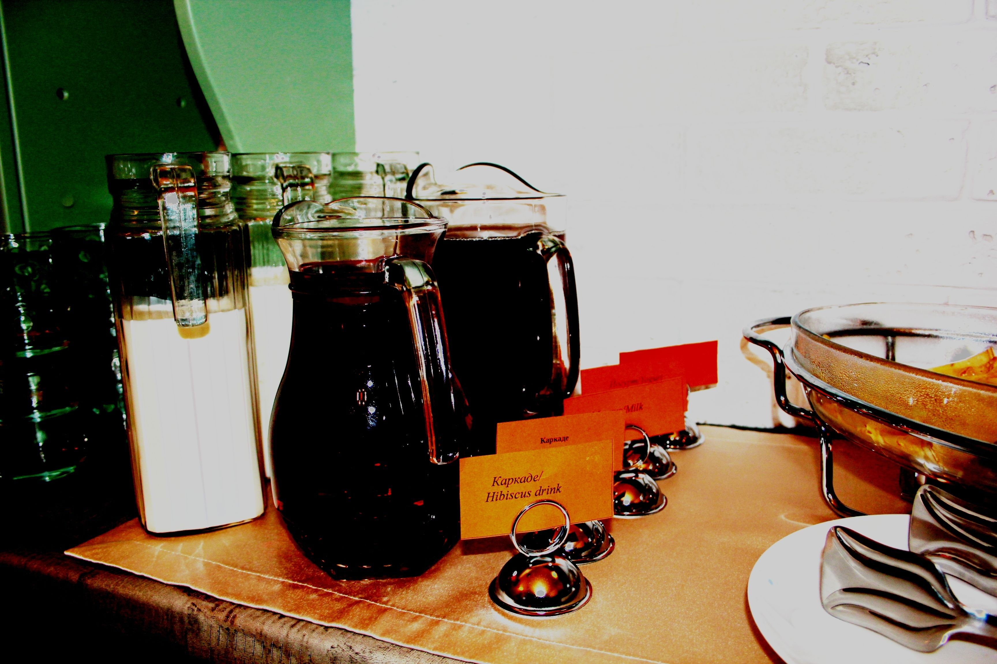 Una mesa de buffet con diversas opciones de bebidas y un letrero que indica 'Karpakae/Bebida de hibisco'.