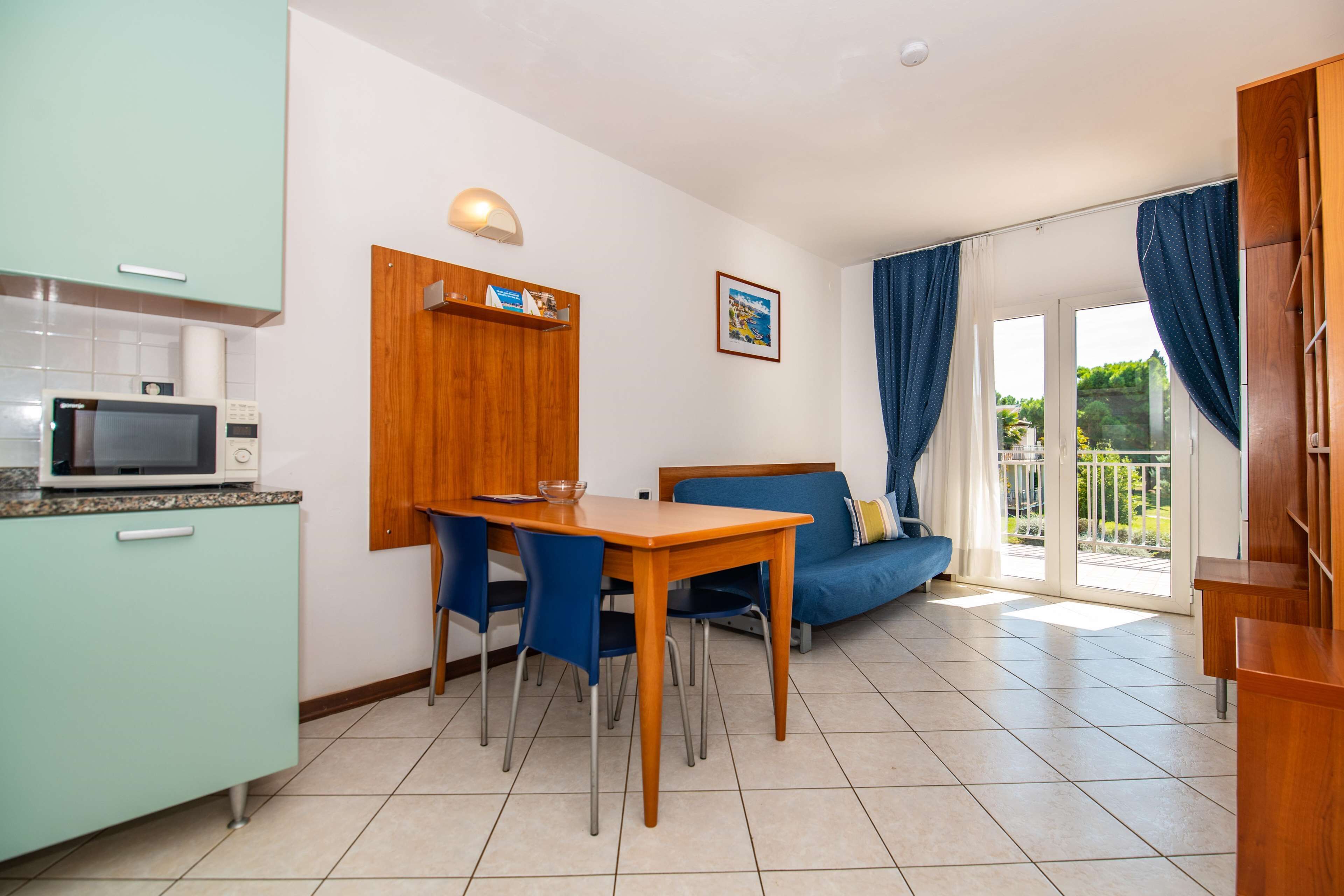 A compact living space with a kitchenette, dining area, and a sofa near a sliding glass door.