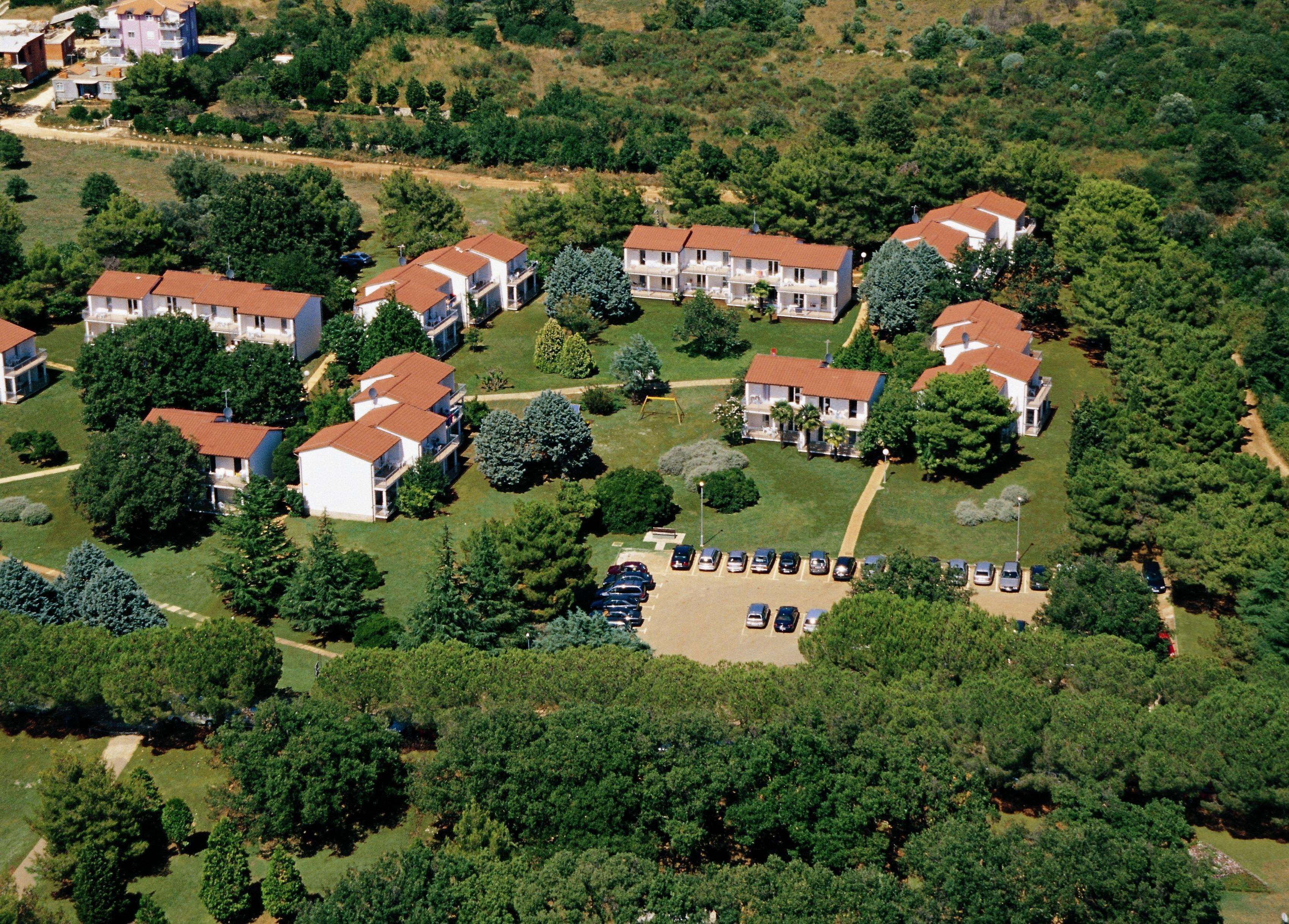 An aerial view of a residential area with multiple two-story houses, a parking lot, and surrounding greenery.