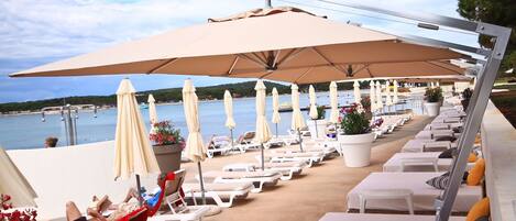 A beachside lounge area with sun loungers and umbrellas, overlooking the sea.