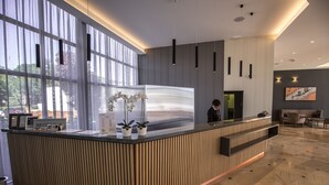 A modern reception desk with vertical paneling, potted plants, and a large window providing natural light. - Ai Pini Medulin Resort (Medulin)