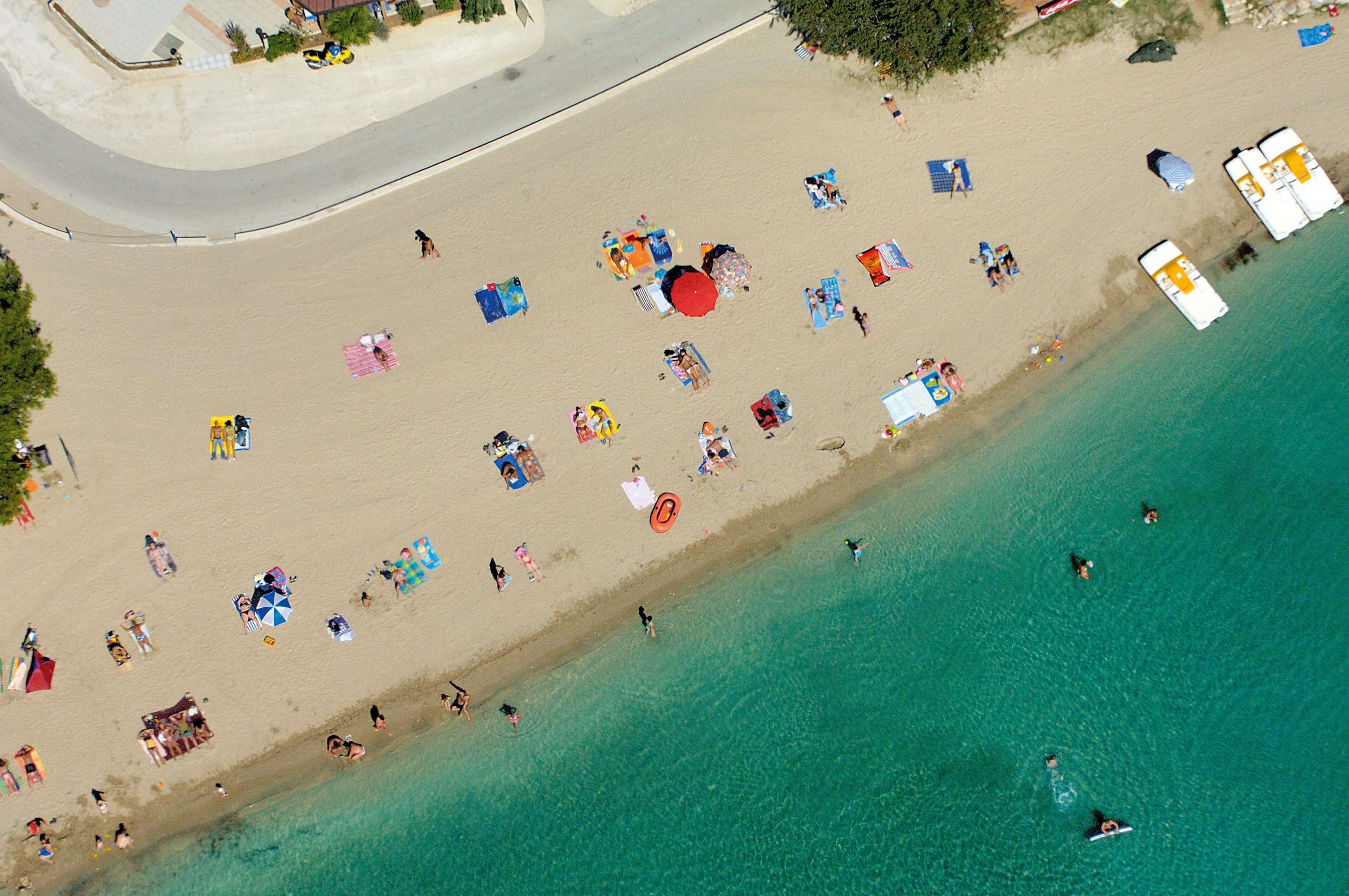 An aerial view of a beach with people sunbathing, swimming, and walking along the shore.