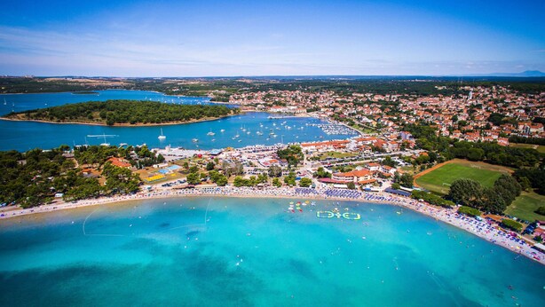 An aerial view of a coastal town with a beach, marina, and residential areas. - Ai Pini Medulin Resort (Medulin)