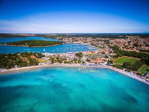 Vista aérea de un pueblo costero con playa, puerto deportivo y zonas residenciales.