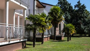A building with a balcony, palm trees, and a clear sky. - Ai Pini Medulin Resort (Medulin)