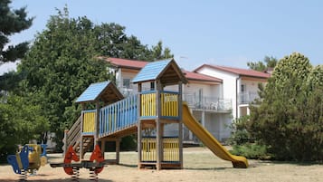 Explore the adjacent playground with a wooden play structure featuring a slide and climbing area, surrounded by lush trees and greenery.