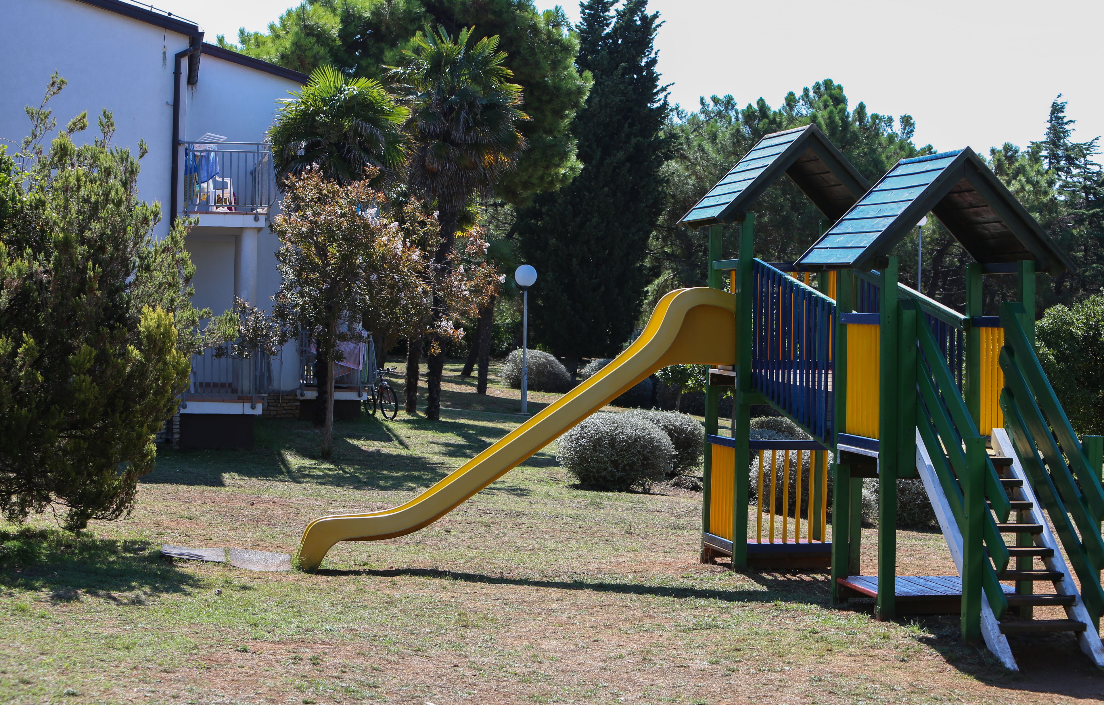 Un parc infantil amb un tobogan groc i una estructura d'escalada verda.