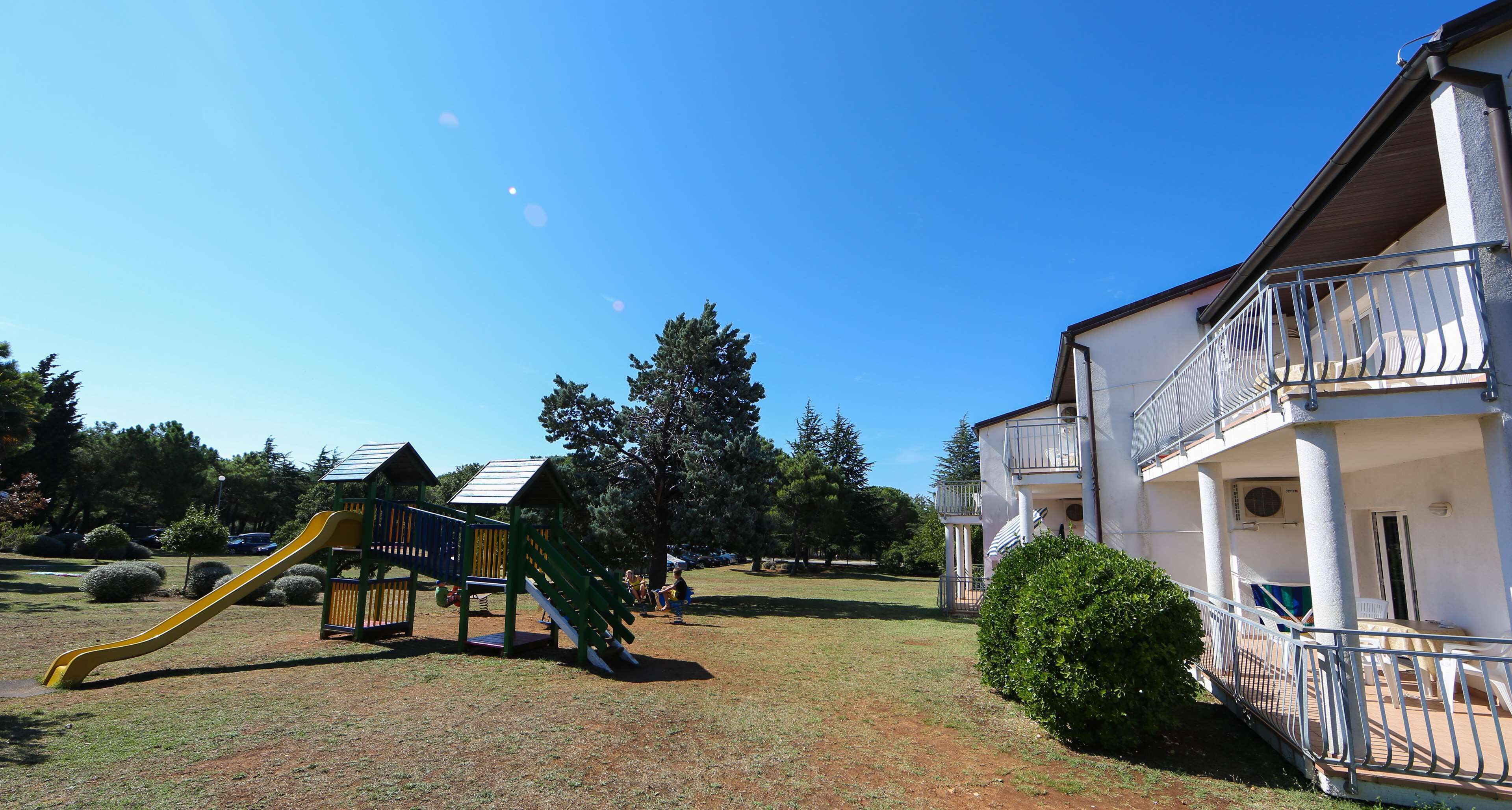 A playground with a slide and climbing structure, surrounded by grass and trees.