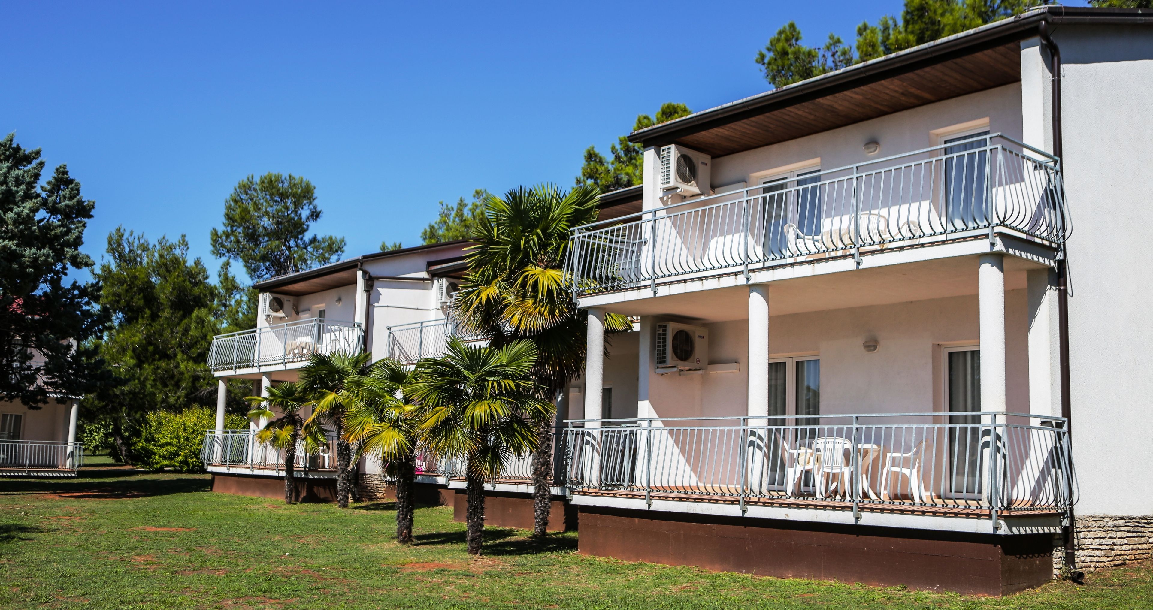 Un immeuble à deux étages doté de balcons, d’une terrasse et de palmiers.
