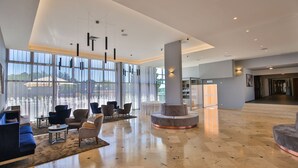 A spacious lobby with a high ceiling, large windows, and modern furniture. - Ai Pini Medulin Resort (Medulin)