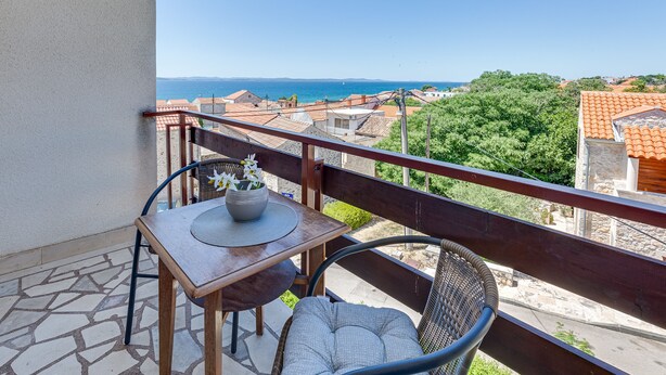 A balcony with a table and chairs, overlooking a coastal view. - Baresic Apartmani (Zadar)