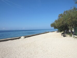 A beach with a pebble path leading to the water, a bench, and a tree line. - Baresic Apartmani (Zadar)