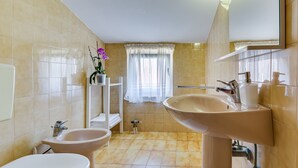 A bathroom with a toilet, bidet, sink, and a window with curtains. - Baresic Apartmani (Zadar)
