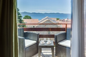 Ein Balkon mit Korbmöbeln, einem kleinen Tisch mit Tassen und einer Teekanne, und Blick auf Meer und Berge.