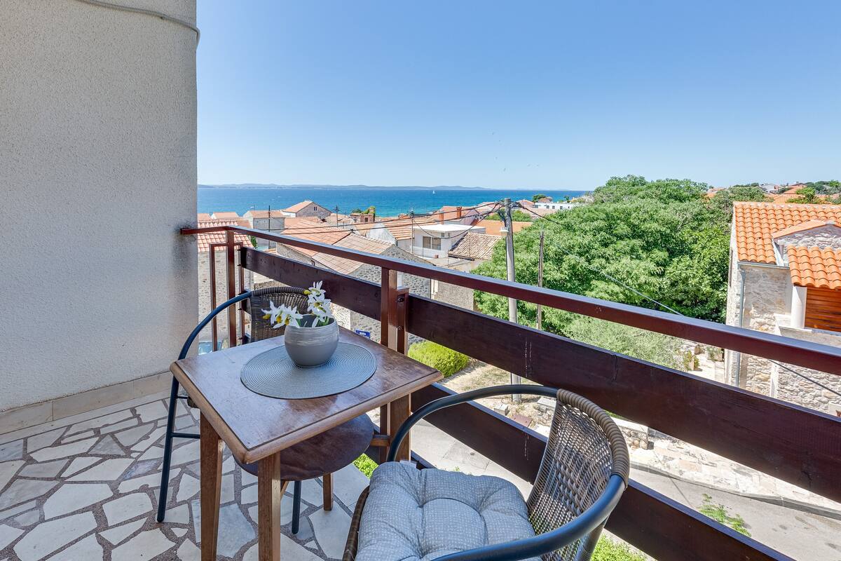 A balcony with a table and chairs, overlooking a coastal view.