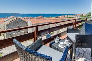 A balcony with wicker furniture, a table with cups and a pitcher, and a view of the sea and buildings.