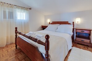 A wooden four-poster bed with white linens, a nightstand with a lamp, and a wooden dresser with drawers.